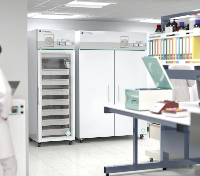 A laboratory with two large medical refrigerators labeled Blood Bank and Plasma, surrounded by lab equipment, colorful sample tubes, and a person in a white lab coat partially visible on the left.